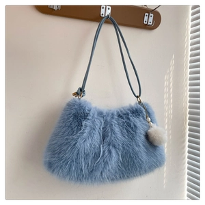 Close-up of light blue faux fur shoulder bag with a soft white pompom charm detail