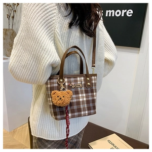 Detail view of plaid shoulder bag featuring puppy embroidery and plush bear pendant accessory