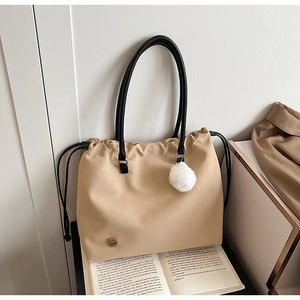 Detail of minimalist beige drawstring tote bag featuring a white plush pompom and black strap