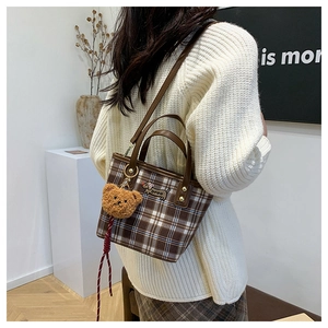 Detail of plaid shoulder bag featuring dog embroidery, plush charm and leather strap