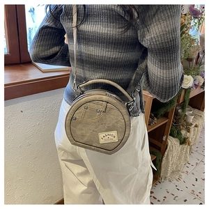 Detail of round khaki crossbody bag with denim pocket design, rivets, and fashion label