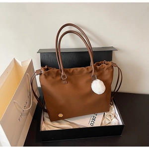 Brown tote bag with pompom charm in a premium gift box detail showing nylon texture