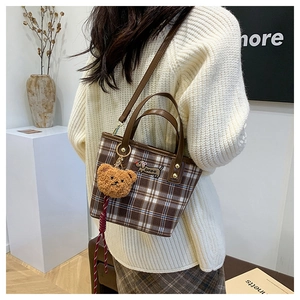 Detail of a brown plaid tote bag with dog embroidery and a cute teddy bear charm