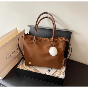 Close-up of caramel brown nylon tote bag with drawstring and white fur ball charm in gift box