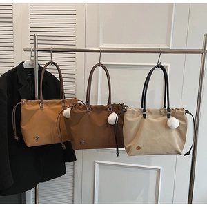 Three minimalist nylon tote bags in beige and brown hanging on a metal rack