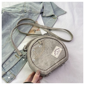 Detail of gray denim-textured round crossbody bag with silver studs and fashion label