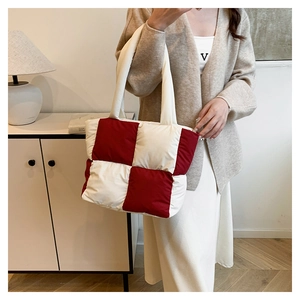 Detail of red and white checkered quilted down tote bag held by model in soft lighting