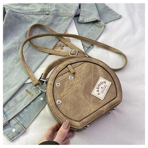 Detail of round brown crossbody bag with denim texture, metal rivets and fabric label