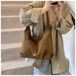 Detail of a brown suede half-moon shoulder bag with a silver oval metal accent at the bottom
