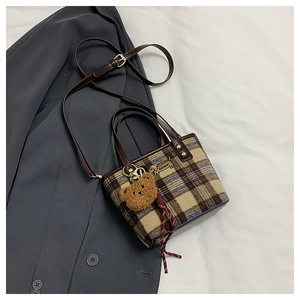 Close-up of wool plaid handbag featuring dog embroidery and a brown plush bear charm