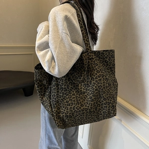 Large leopard print canvas tote bag shown on model in a modern indoor setting