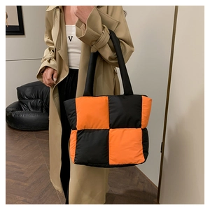 Detail of a large puffer tote bag in black and orange color block on model shoulder
