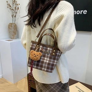 Brown plaid crossbody bag with dachshund patch and plush bear charm in a lifestyle setting