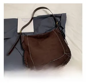 Macro detail of brown suede saddle bag with hand-woven edges and white contrast stitching