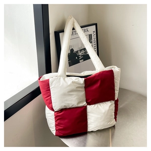 Detail of red and white checkered quilted tote bag with padded strap on a metal table
