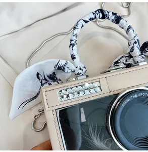 Detail of camera-shaped crossbody bag with rhinestone border and silk scarf handle