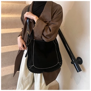 Detail of black suede saddle bag with contrasting white stitching and gold buckle