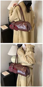 Close-up of a vintage dark reddish-brown leather cylinder shoulder bag with a small pouch
