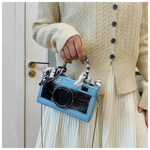 Detail of camera-shaped crossbody bag with silk scarf handle and metal chain strap