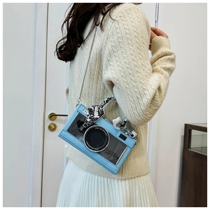 Detail of light blue camera-shaped crossbody bag with silver chain and silk scarf