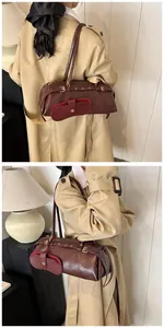 Detail of dark brown leather baguette bag with metal buckles and side zipper pouch
