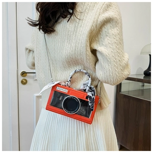 Detail of bright orange camera-shaped crossbody bag with silver chain and silk scarf