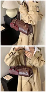 Detail of a dark brown leather barrel bag with metallic buckles and small side pouch