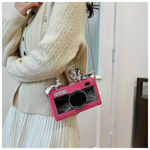 Detail of pink camera-shaped crossbody bag with decorative scarf and feather accents