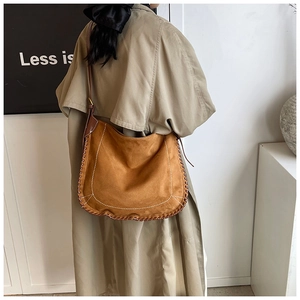 Detail of caramel suede saddle bag featuring hand-woven edges and white stitching