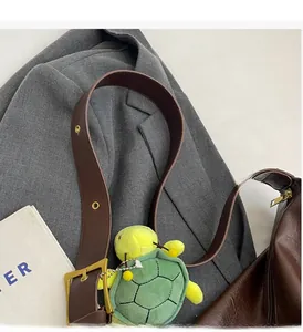 Brown leather tote bag with thick strap and a cute green turtle plush pendant detail