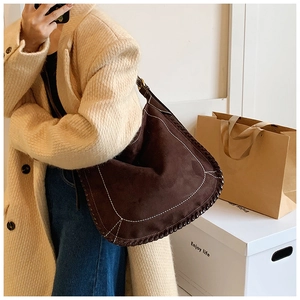 Detail of a brown suede tote bag with white contrast stitching and woven leather trim