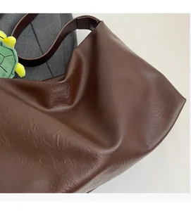 Detail of brown leather tote bag texture featuring wide strap and green turtle charm