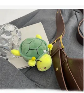 Detail view of a green and yellow plush turtle bag charm with a metal chain hanger