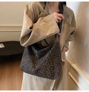 Detail of a leopard print crescent tote bag with wide shoulder strap worn with a trench coat