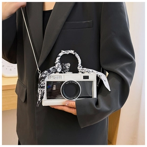 Close-up of camera-shaped bag with rhinestones and silk scarf handle worn by a model