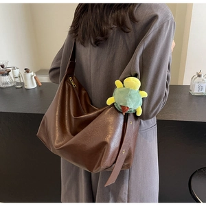 Detail of dark brown leather hobo bag with wide shoulder strap and green dinosaur charm