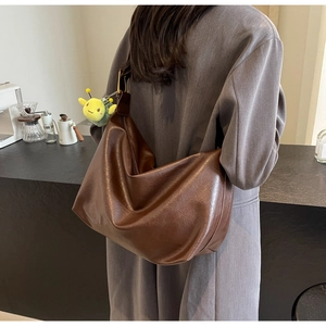 Detail of dark brown leather tote bag with yellow bee plush charm on the shoulder strap