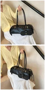 Detail of black leather baguette bag with metal buckles and small round pouch