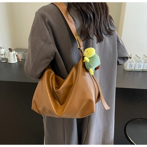 Detail of vintage brown leather tote bag with a cute green turtle plush charm accessory
