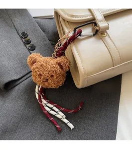 Detail of a brown fuzzy bear bag charm with red and white tassels on a beige handbag