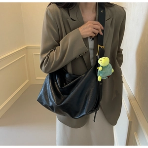 Detail of black leather crescent bag featuring metal eyelets and green plush turtle charm