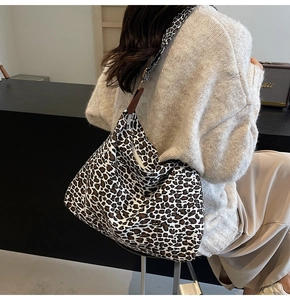 Detail view of a large leopard print canvas tote bag worn by a model in casual knitwear
