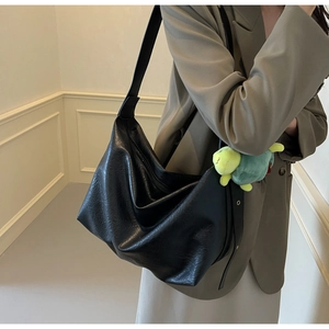 Detail of black hobo bag with pleated leather texture and a green turtle plush charm