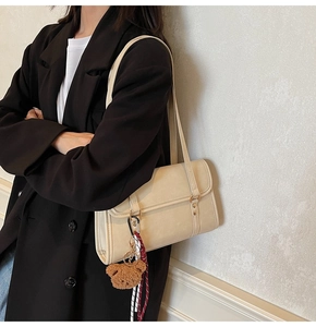 Detail of cream rectangular shoulder bag featuring a cute plush bear charm and woven cord