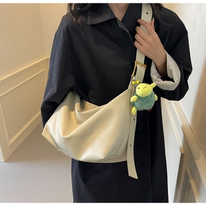 Detail of cream leather hobo bag with wide strap and green plush bug charm