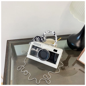 Detail of camera-shaped crossbody bag with rhinestone lens and silk scarf handle decor