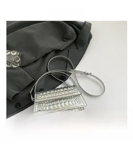 Detail of silver crocodile-embossed crossbody bag with metallic finish and top handle