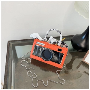Detail of camera-shaped crossbody bag featuring orange lens and silk scarf wrap