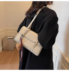 Close-up of cream square shoulder bag with plush pendant and checkered scarf detail