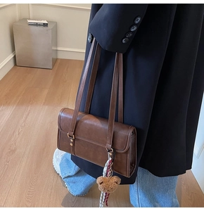 Detail of dark brown leather baguette bag with plush bear charm and woven rope